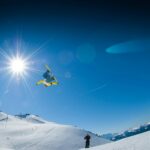 Snowboarder executing a freestyle trick in the sunny winter Alps.